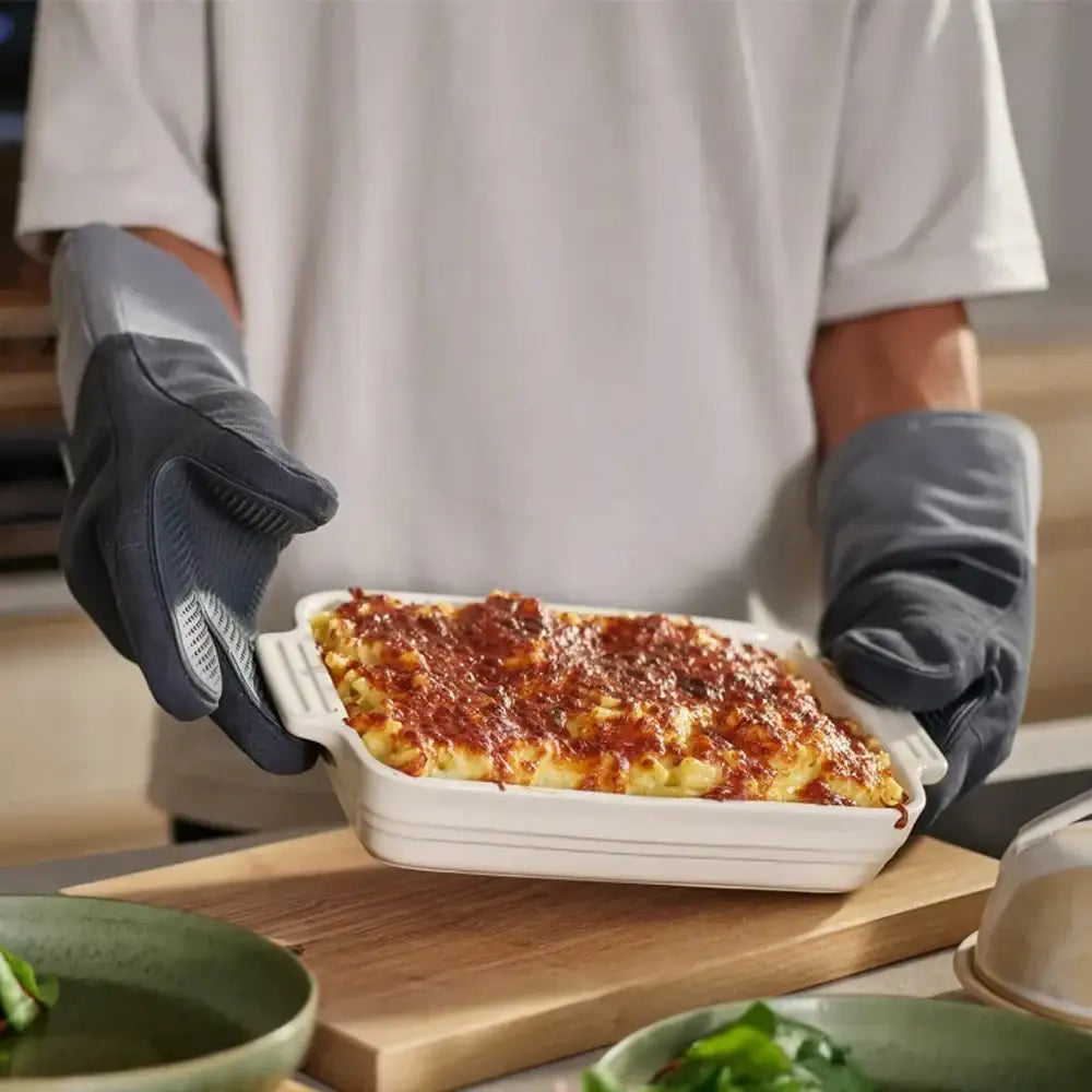 Person holding a dish of baked mac and cheese in a kitchen setting