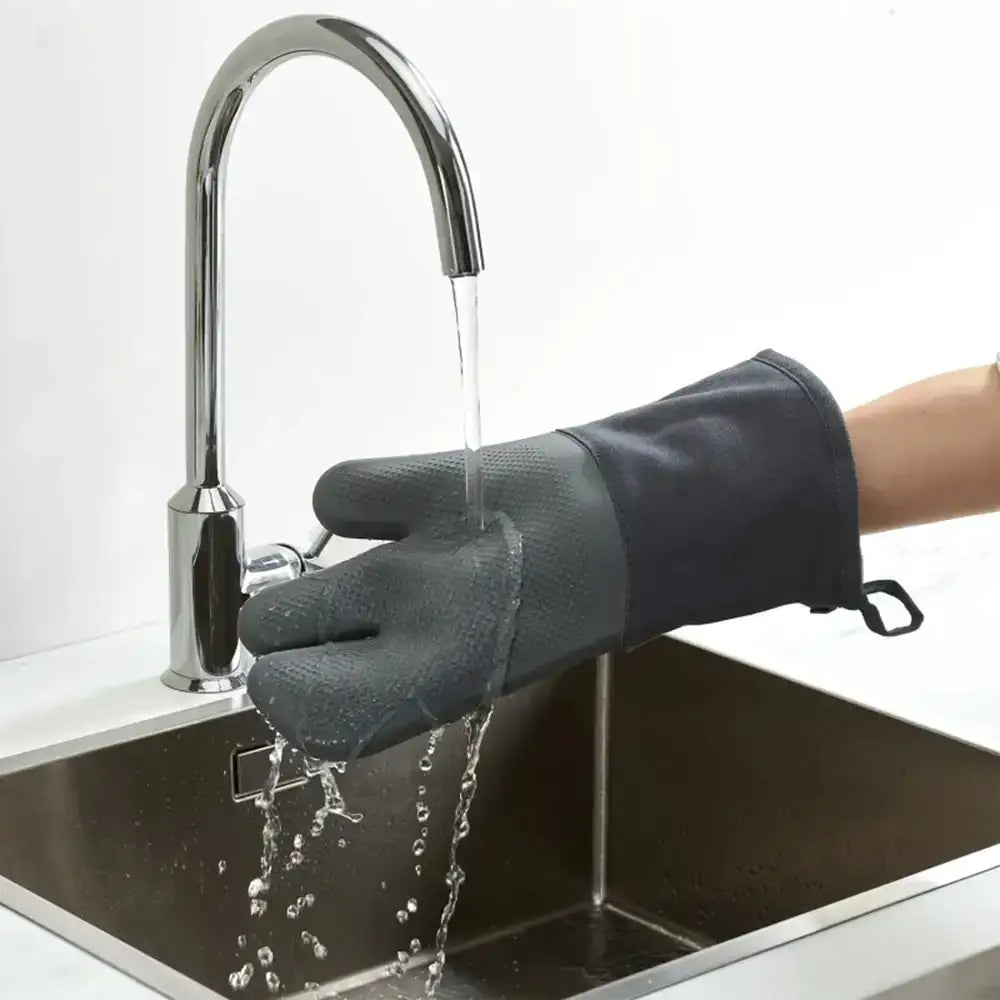 Person washing hands with a black glove in a kitchen sink.