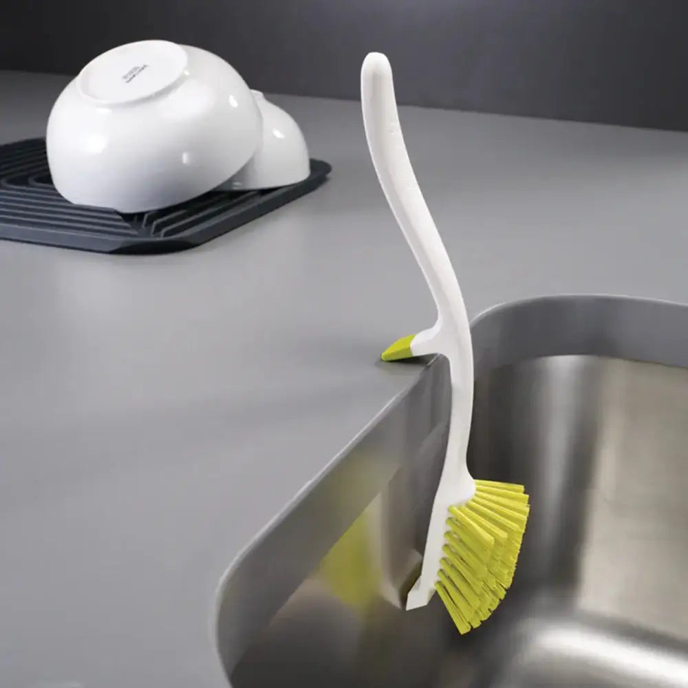 Kitchen brush with yellow bristles on a kitchen counter next to a sink.