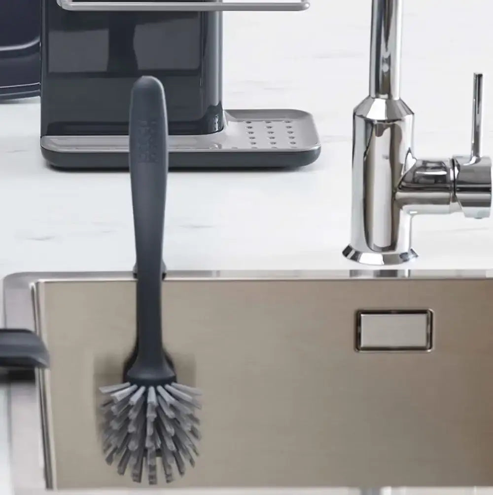 Gray kitchen brush on a kitchen counter with a faucet and sink in the background.