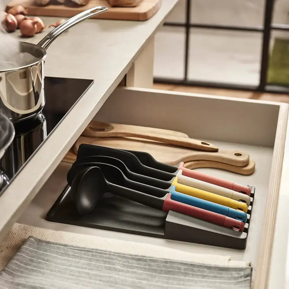 Set of colorful ladles in a kitchen drawer with wooden utensils.