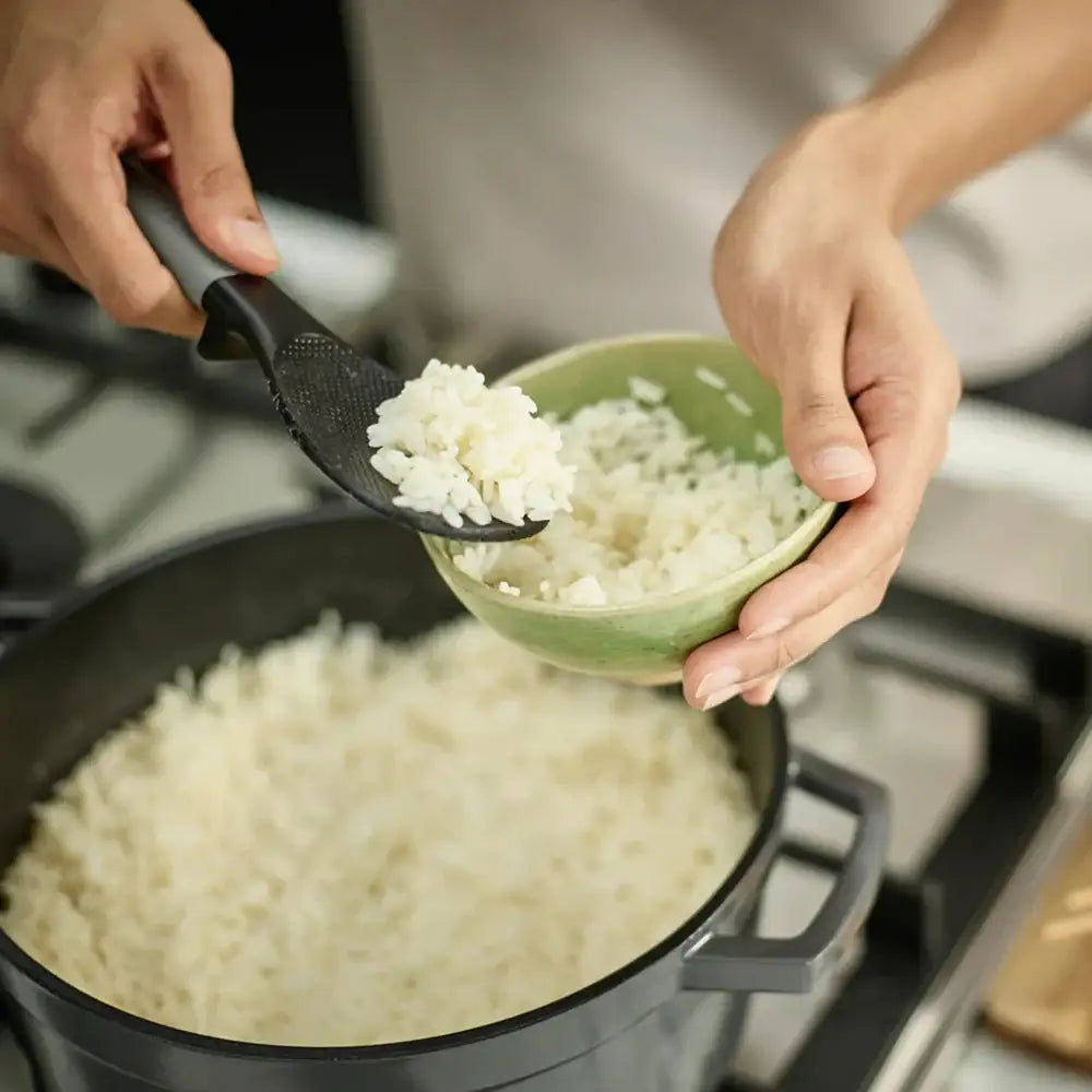Person scooping rice from a pot into a green bowl using a black spoon.