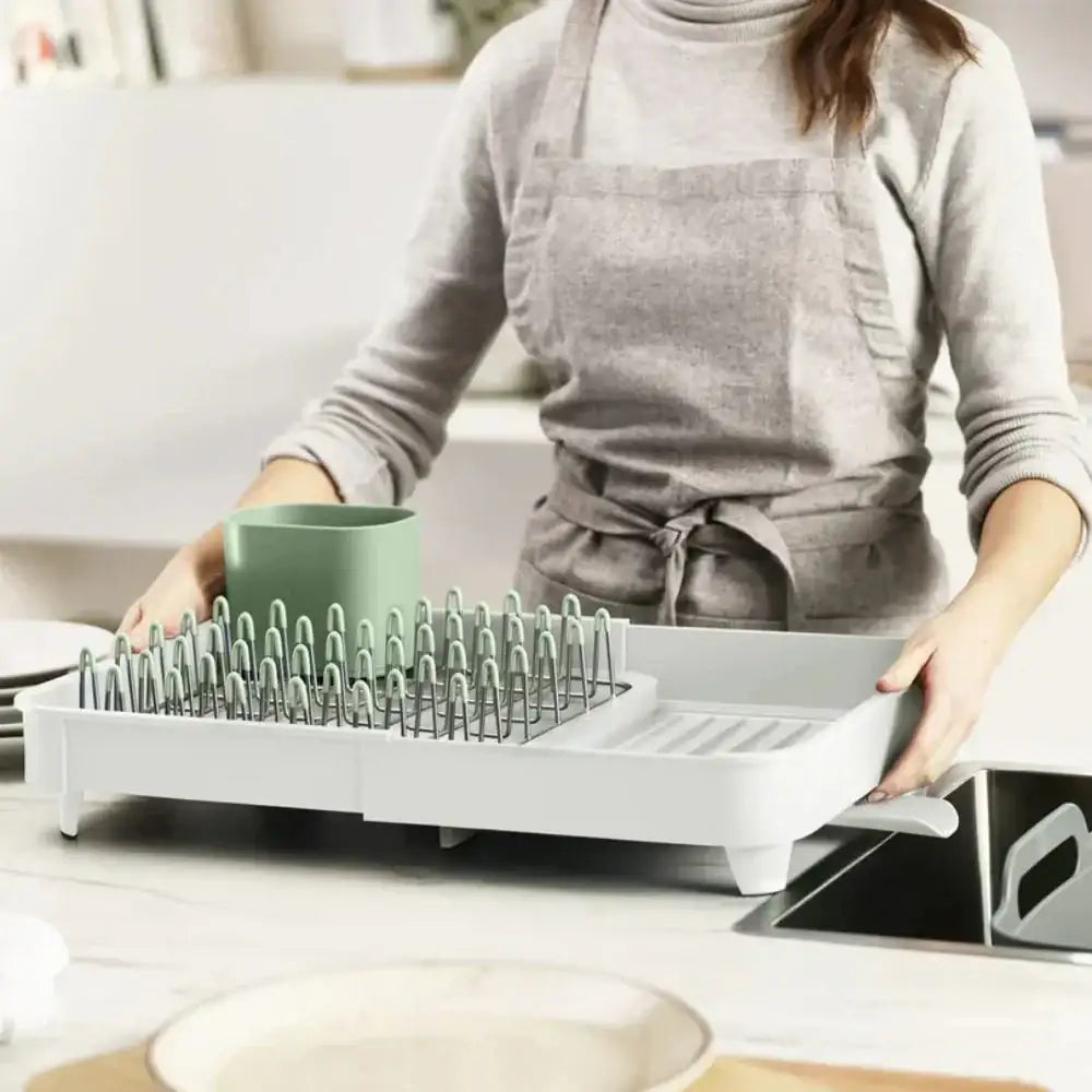 Person using a white dish drying rack with green cup in a kitchen setting