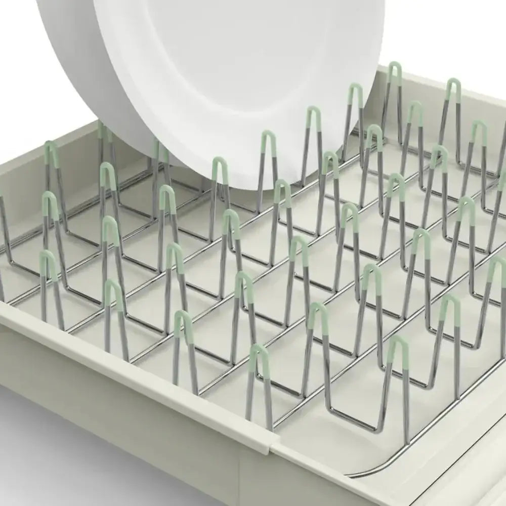 Dish rack with green clips holding a white plate on a light gray background