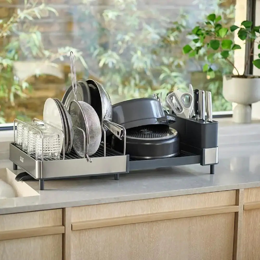 Dish rack with dishes on a kitchen counter near a window with plants outside