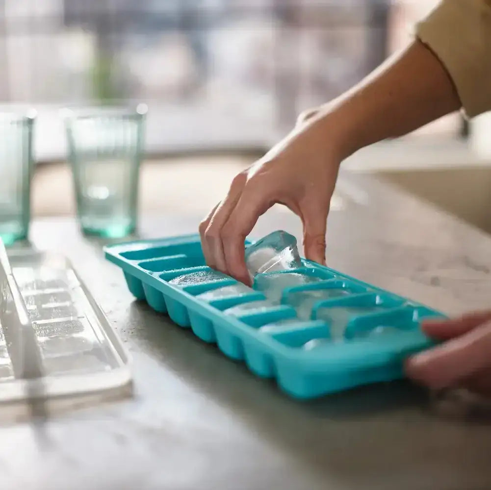 Person filling a teal ice cube tray with water on a kitchen counter.