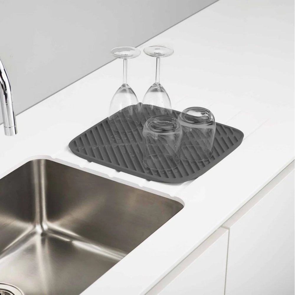 Gray silicone mat on a kitchen counter with glasses and a sink.