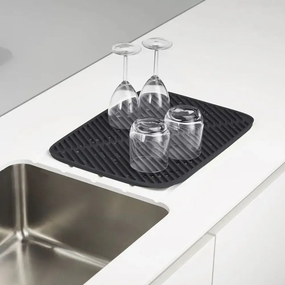 Black silicone mat with glasses on a kitchen counter next to a sink