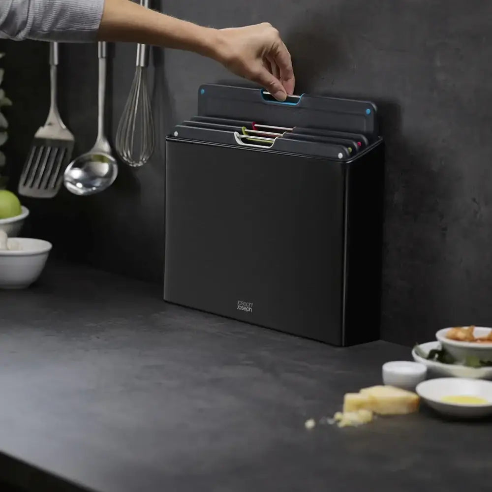 Black kitchen storage box with a hand reaching to open it on a dark countertop.