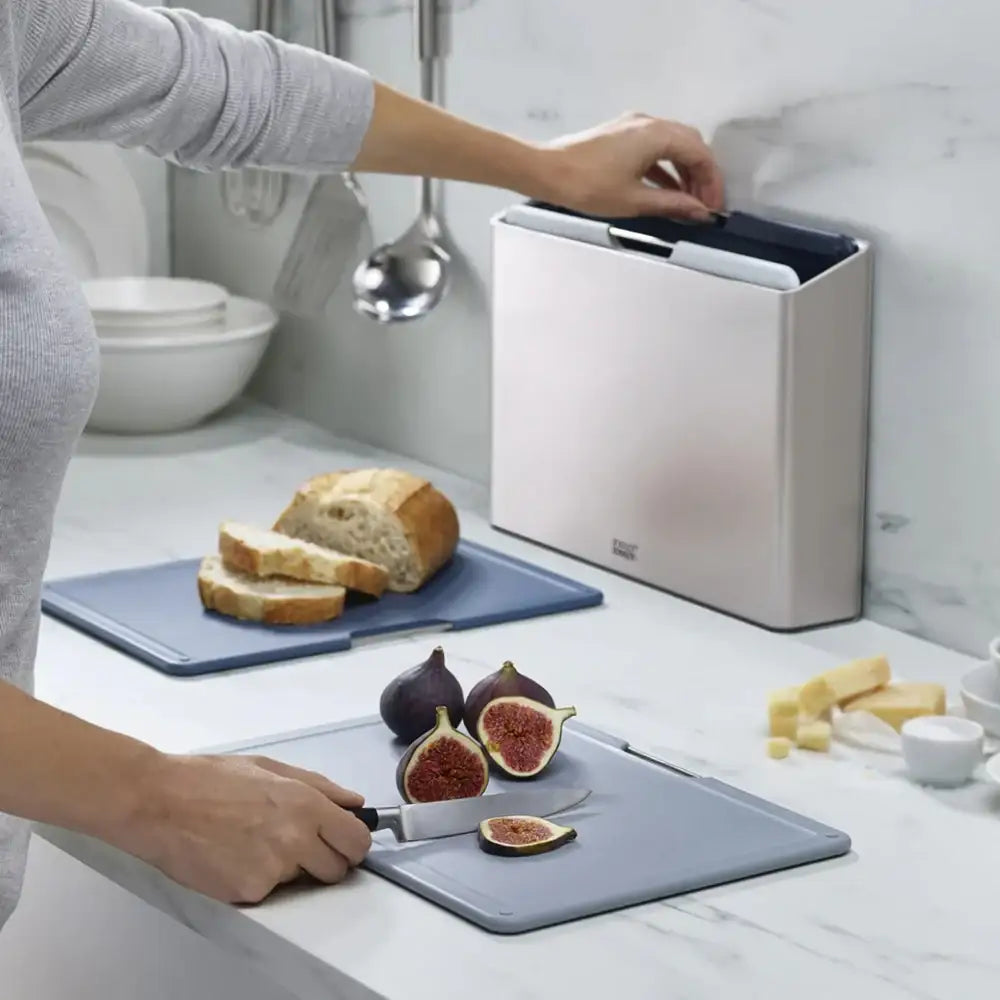 Person cutting figs on a kitchen counter with a knife, surrounded by bread and cheese.