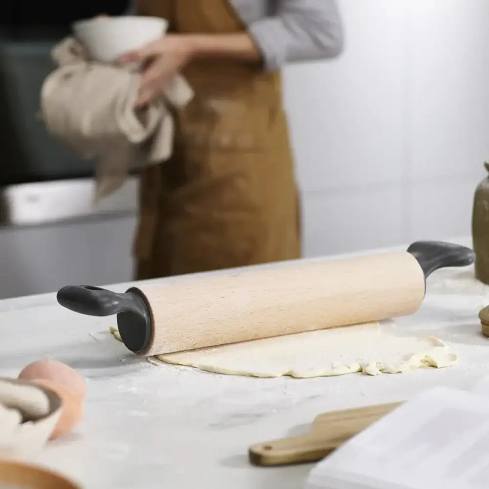 Person in a kitchen with a rolling pin and dough on a table