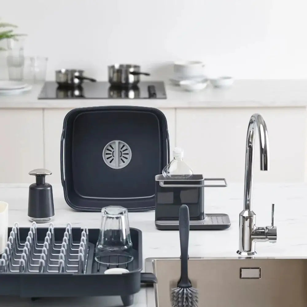 Black dish rack with kitchen items on a white countertop next to a sink.