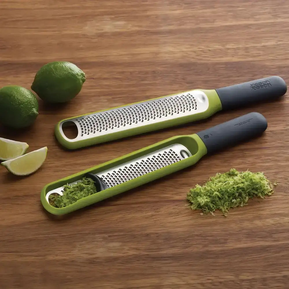 Two green and gray graters on a wooden surface with lime and zest.