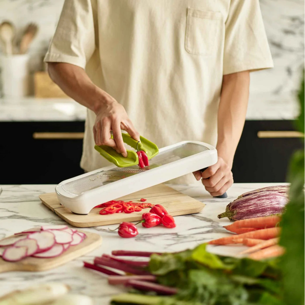 Person using a vegetable peeler on a cutting board with vegetables on a kitchen counter.