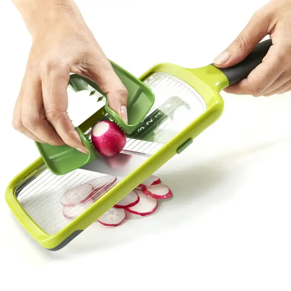 Person using a green vegetable slicer to cut radishes on a white background