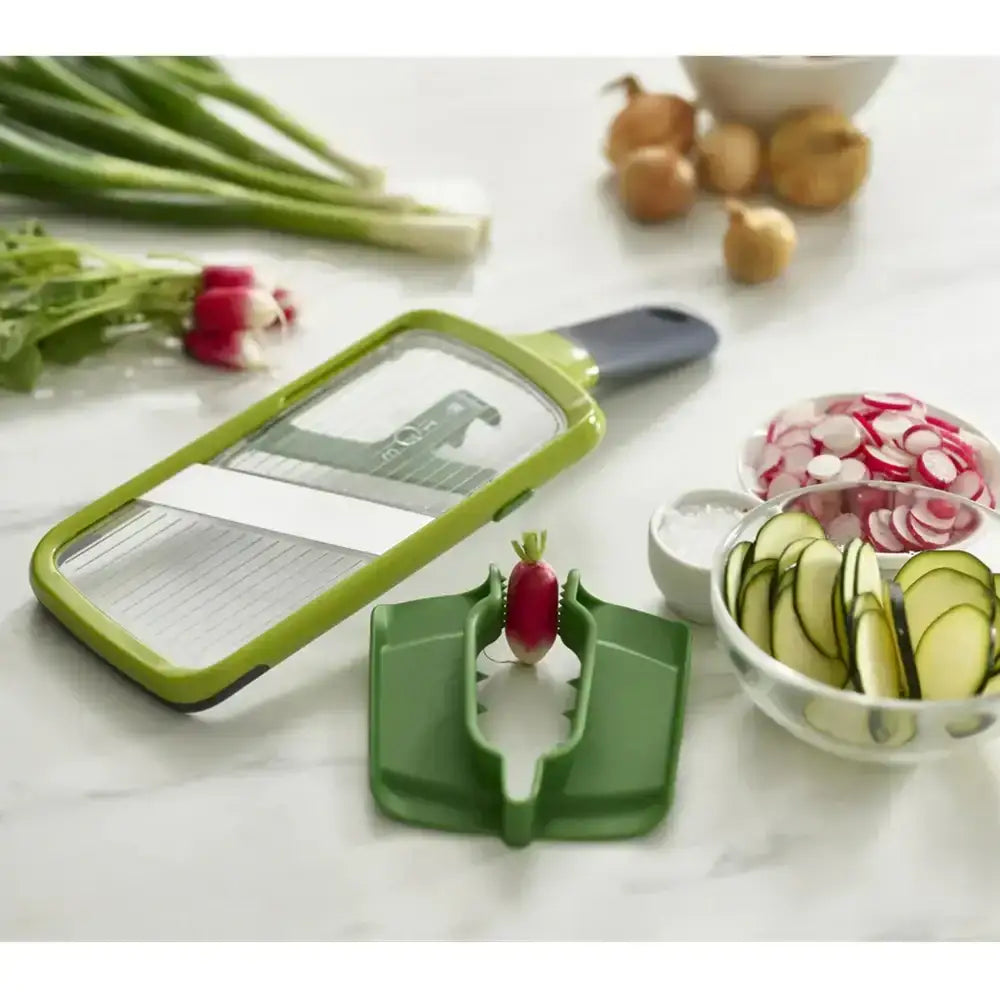 Green vegetable slicer with sliced vegetables on a marble surface