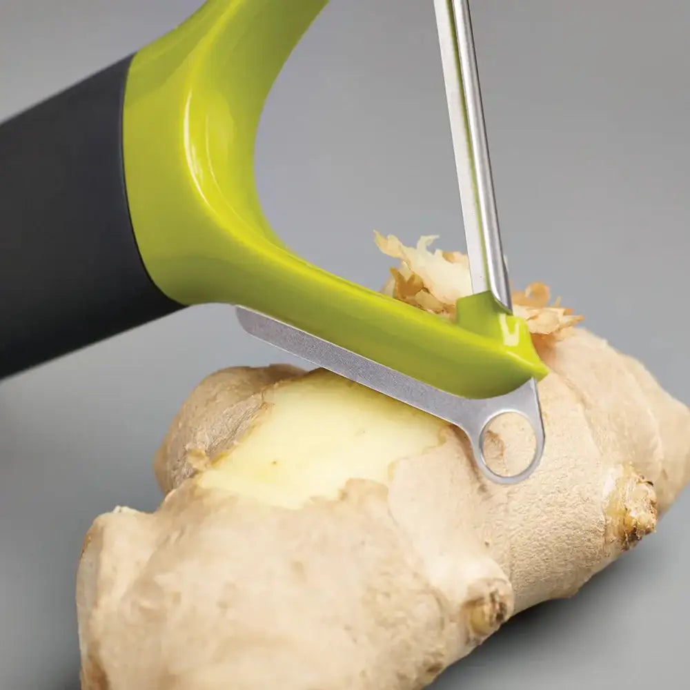 Green ginger peeler being used on a piece of ginger against a gray background