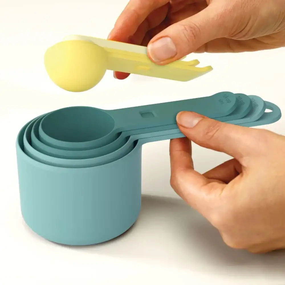 Set of teal measuring cups with a hand holding a yellow spoon over them on a white background