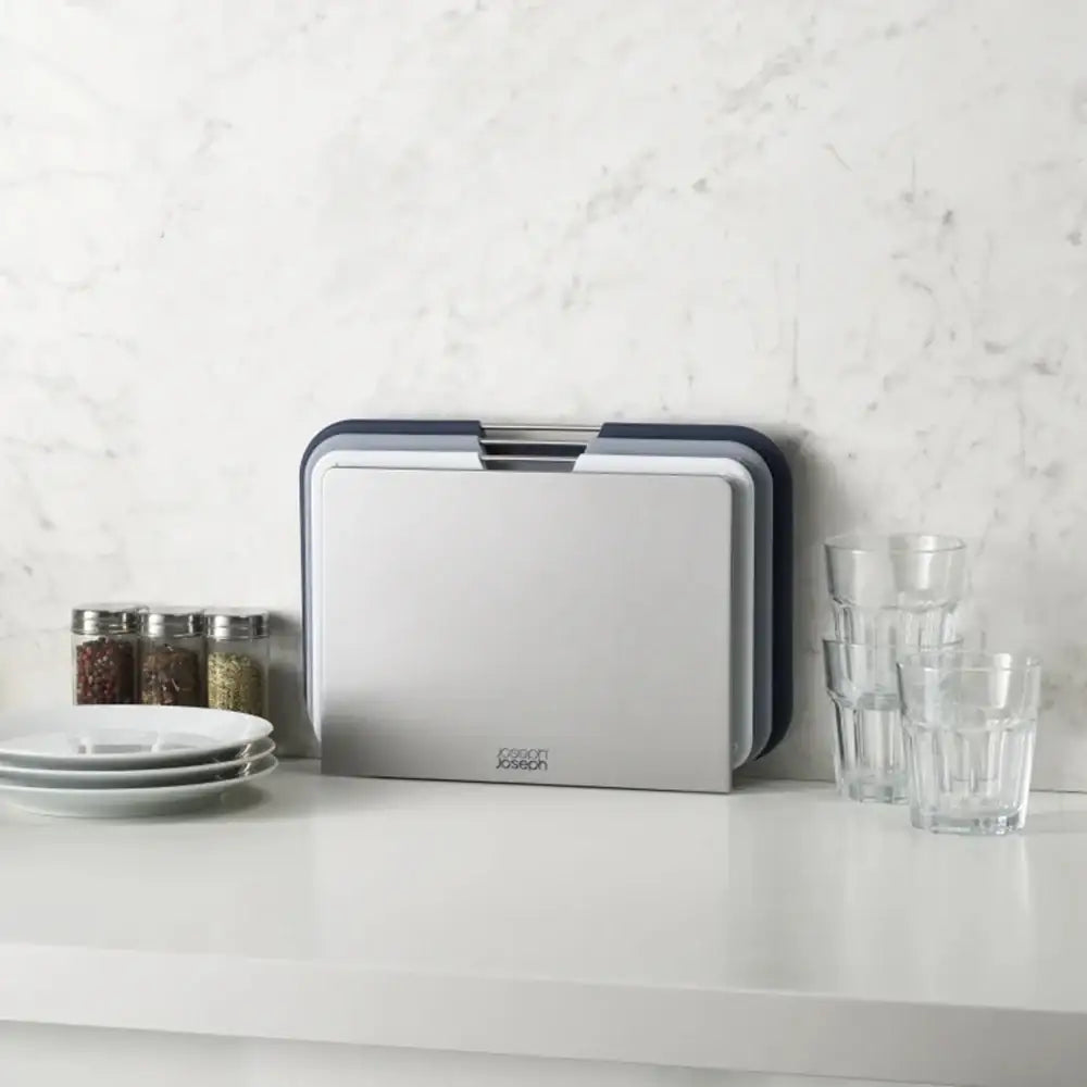 Kitchen countertop with a cutting board, glasses, and plates against a white marble wall.