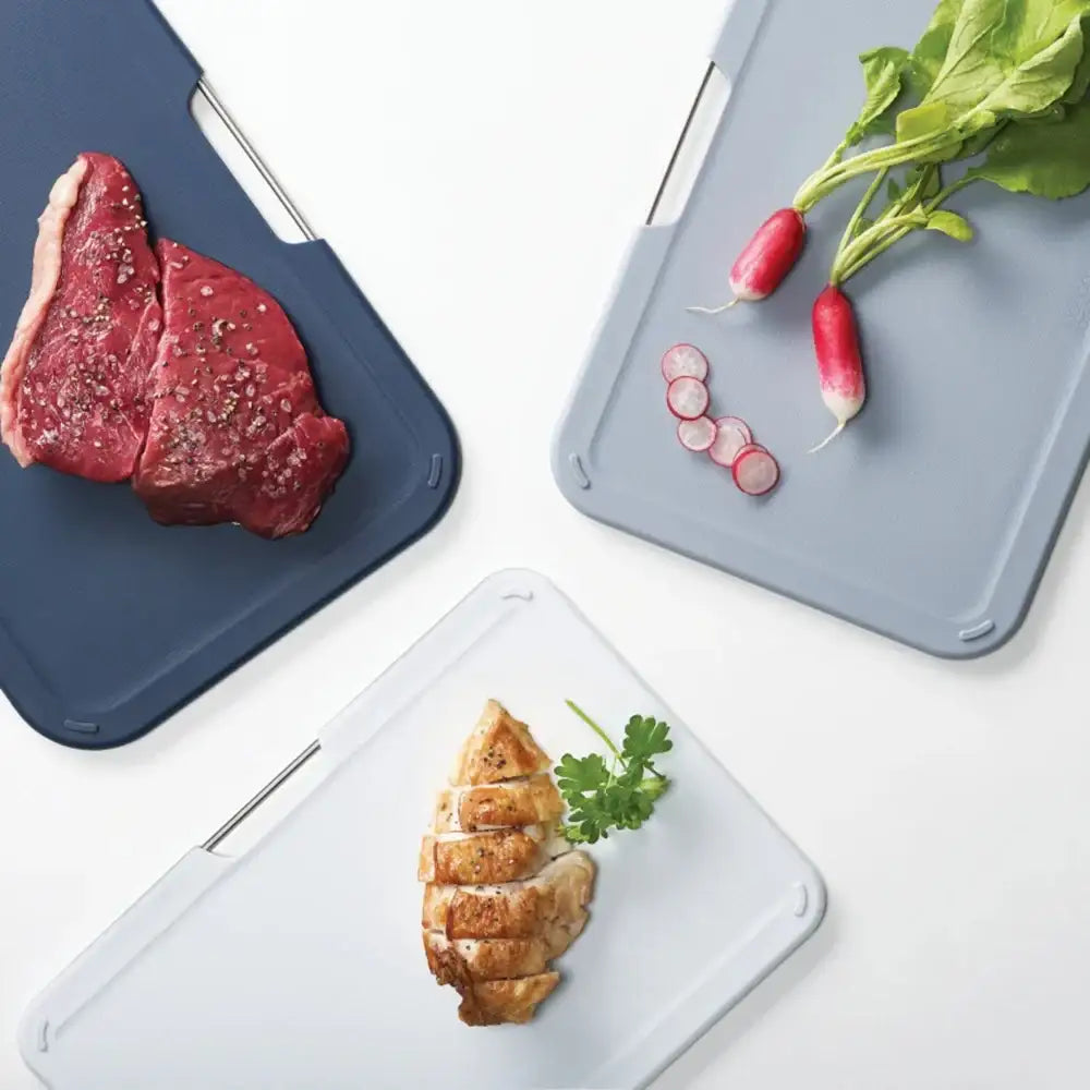 Three cutting boards with raw meat, cooked chicken, and vegetables on a white background
