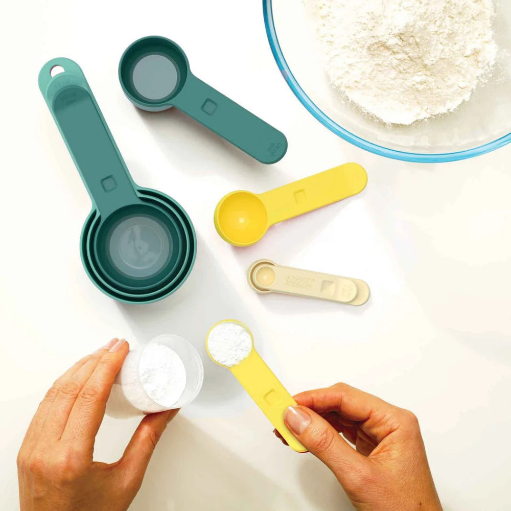 Blue and yellow measuring spoons laid out on a white counter with a bowl of flour 