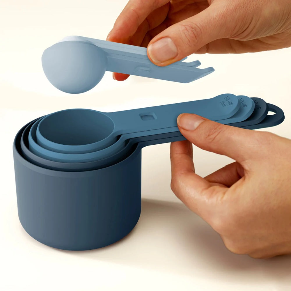 Set of blue measuring cups and spoons held by hands on a light background