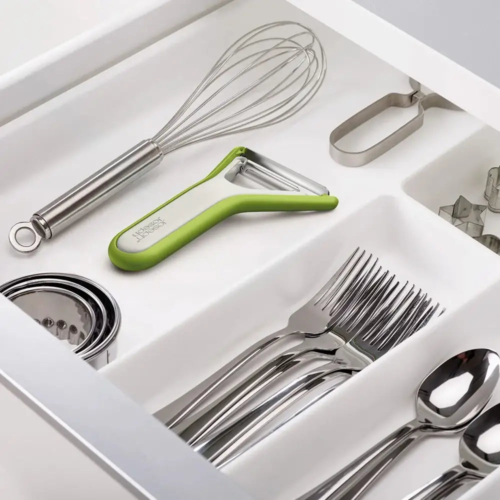 Open kitchen drawer with utensils including a whisk, peeler, and cutlery.