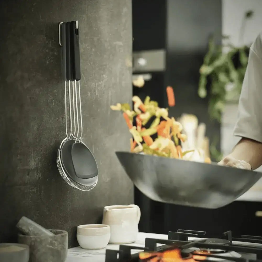 Cooking scene with a wok and hanging measuring cups on a kitchen wall.