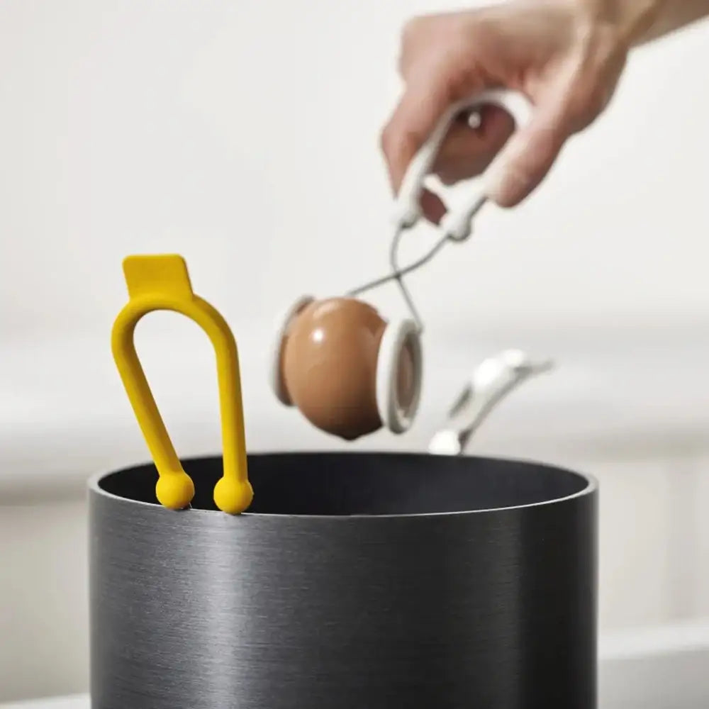 Person using a white spoon to scoop something from a black container with a yellow handle.