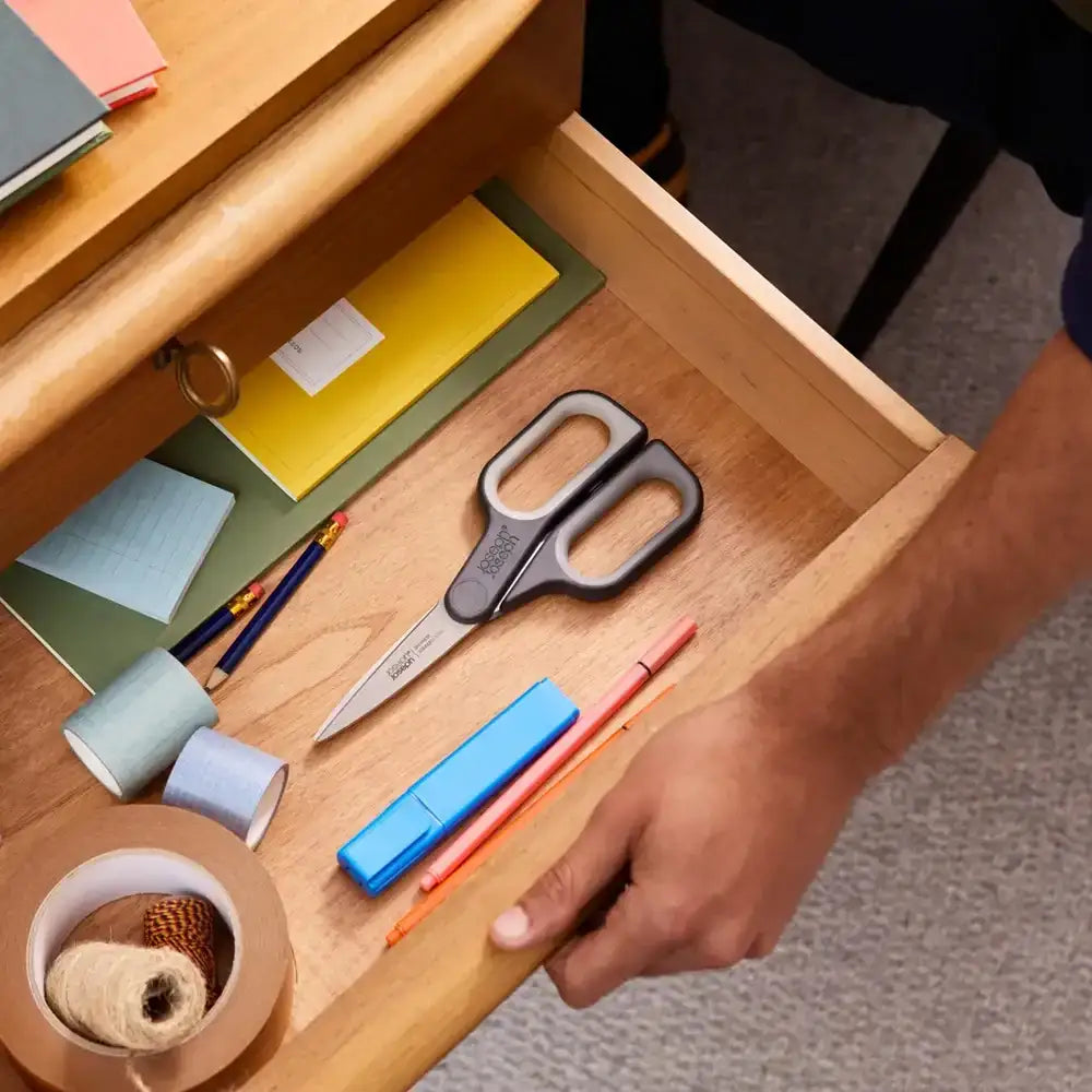 Open wooden drawer with stationery items including scissors, pens, and tape.