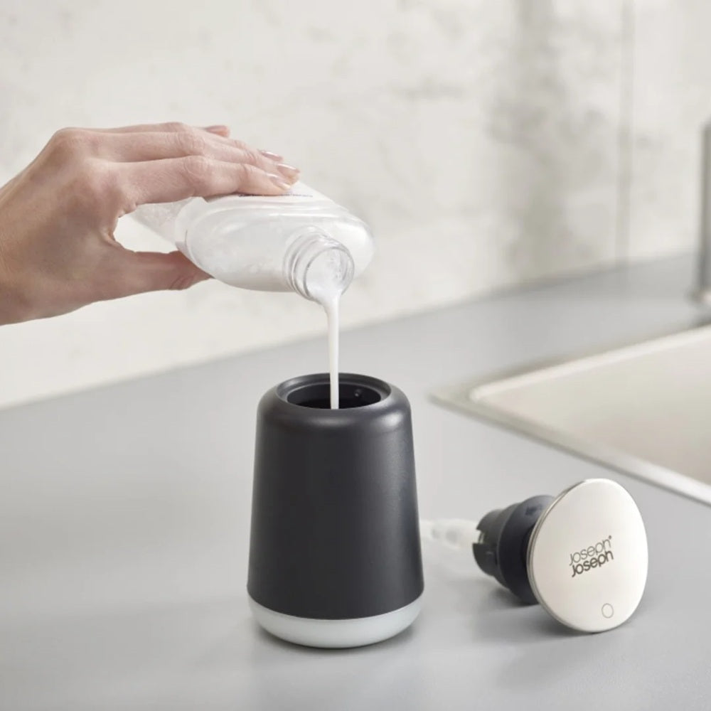 Hand pouring soap into a black and white dispenser on a bathroom counter.
