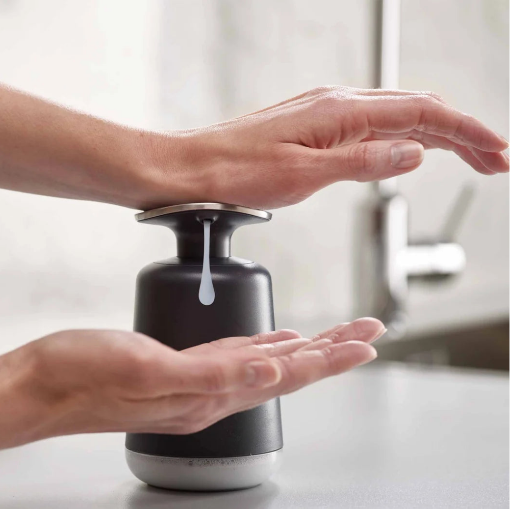 Person using a black soap dispenser to apply soap to their hands.