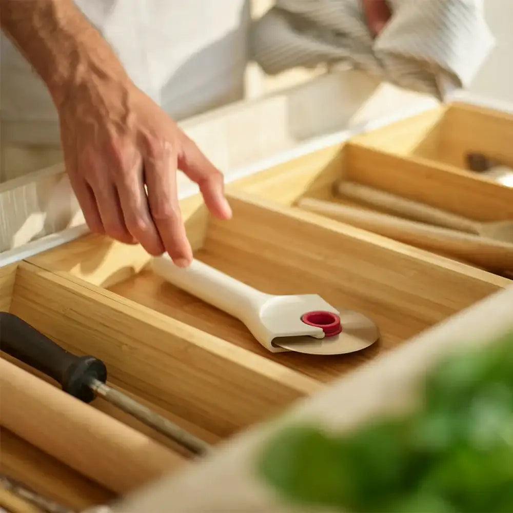 Hand reaching for a white kitchen tool with red accent on a wooden shelf.