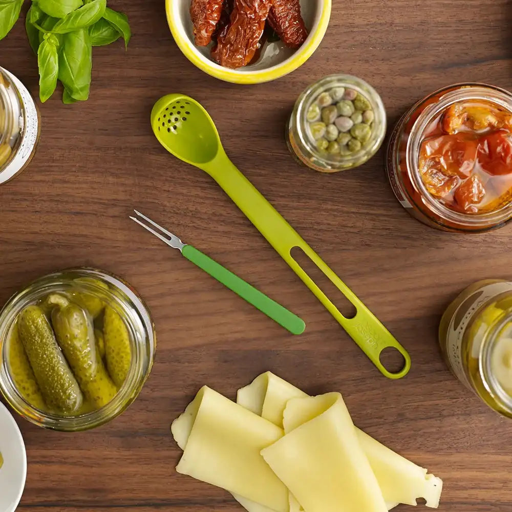 Wooden table with jars of pickles, cheese, and a green ladle.