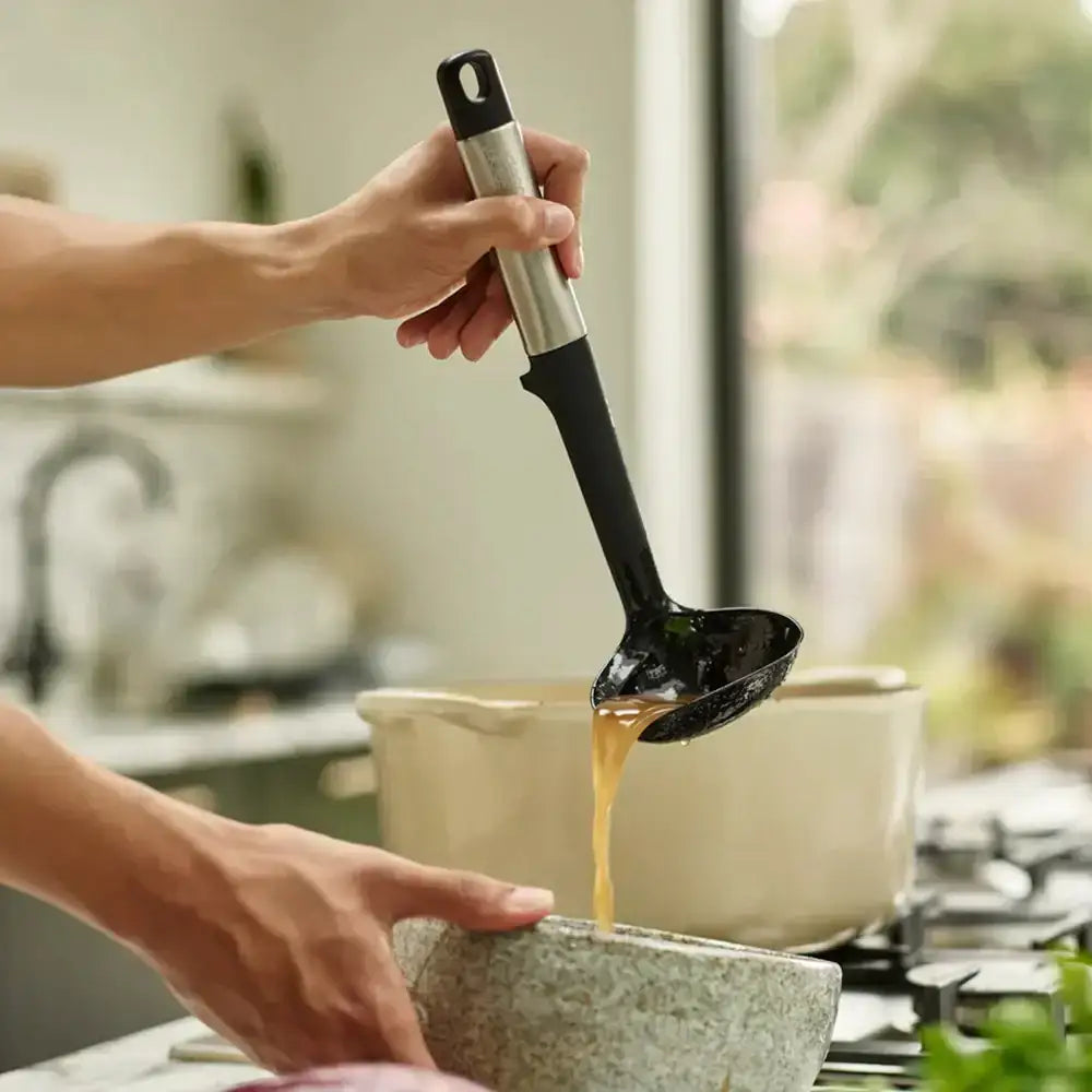 Person using a ladle to pour liquid from a pot into a bowl in a kitchen setting.
