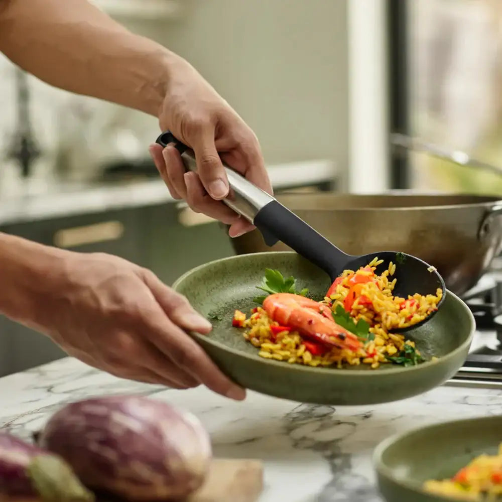 Person serving a dish of food from a green plate with a black spoon.