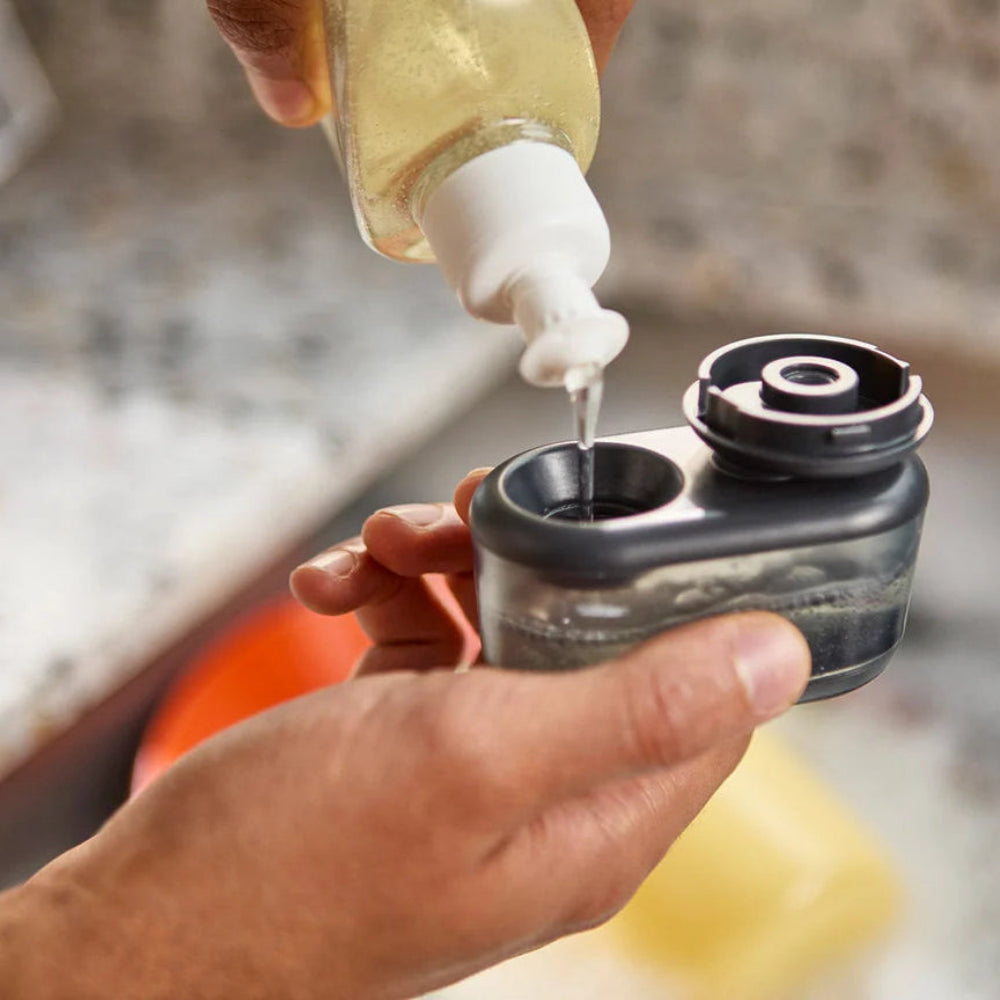 Person filling a soap dispensing brush with dish soap