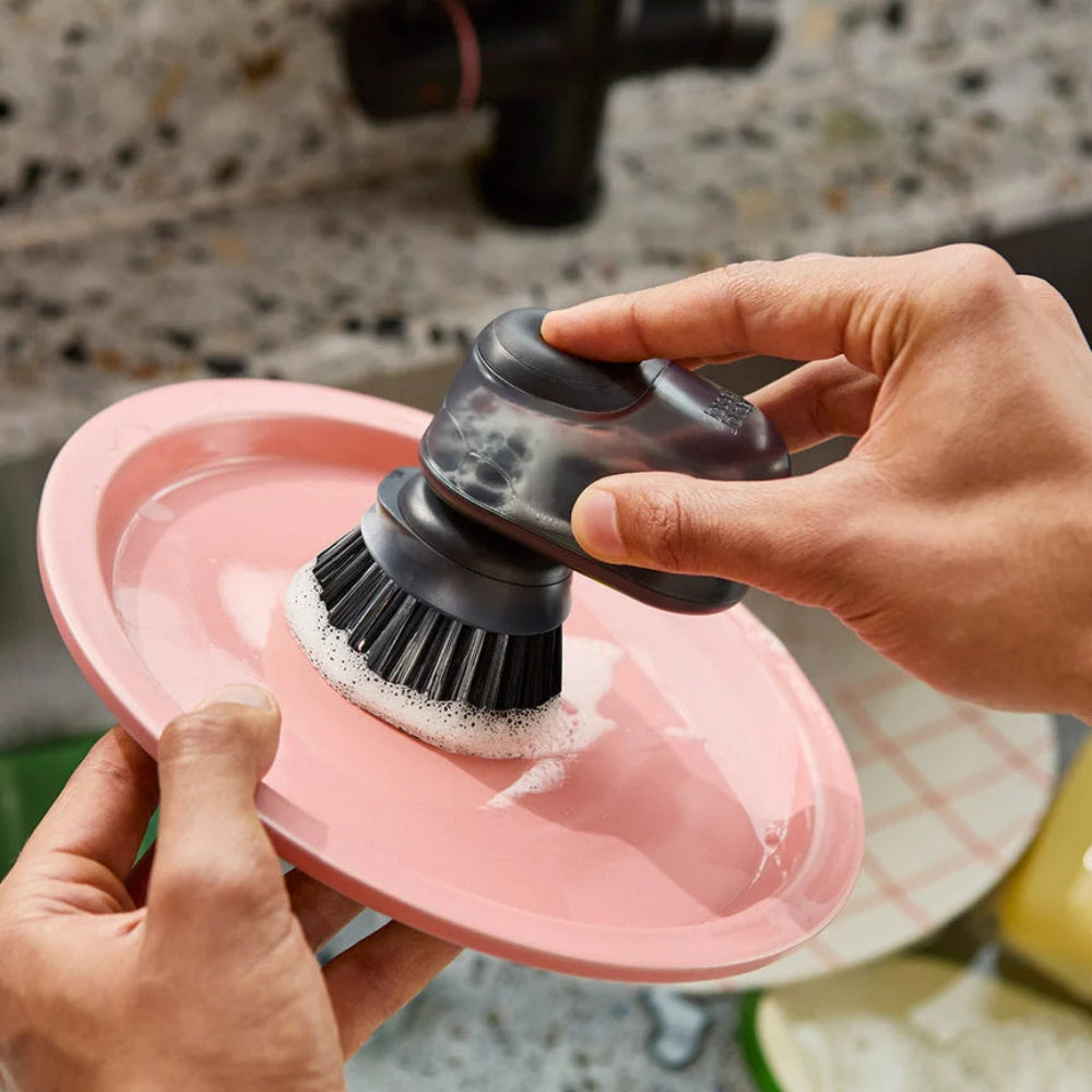 Person using a scrubbing brush on a pink plate 