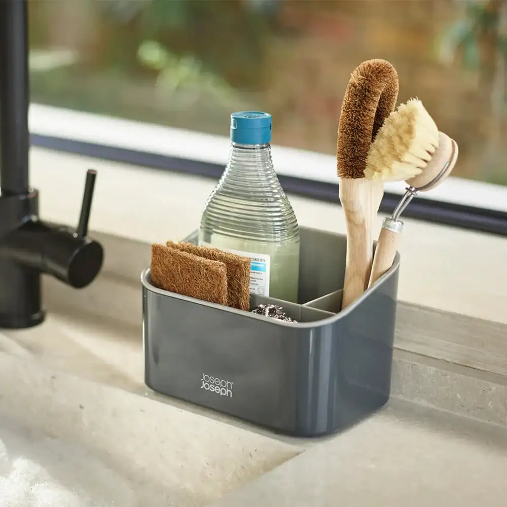 Gray Joseph Joseph sink caddy with cleaning tools on a kitchen counter.
