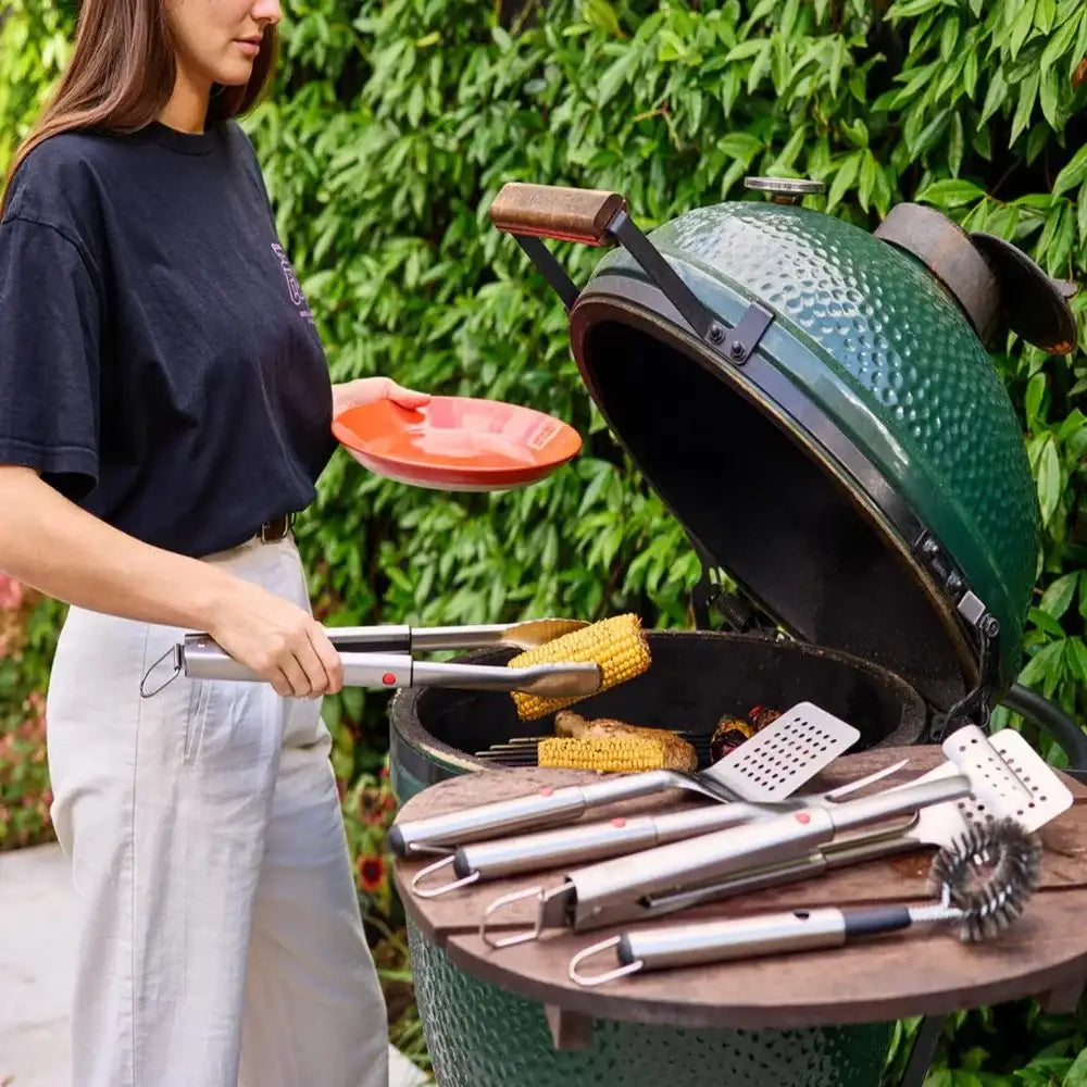 Person using a green barbecue grill with utensils in an outdoor setting
