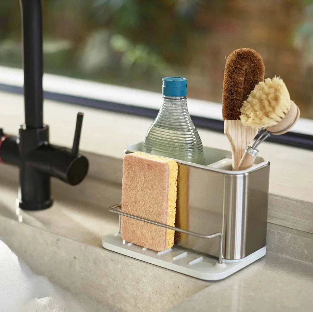 Kitchen sink caddy with sponge, brush, and bottle on a kitchen counter.