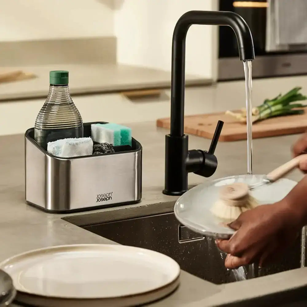 Person washing dishes in a kitchen with a black faucet and Joseph Joseph dish rack.