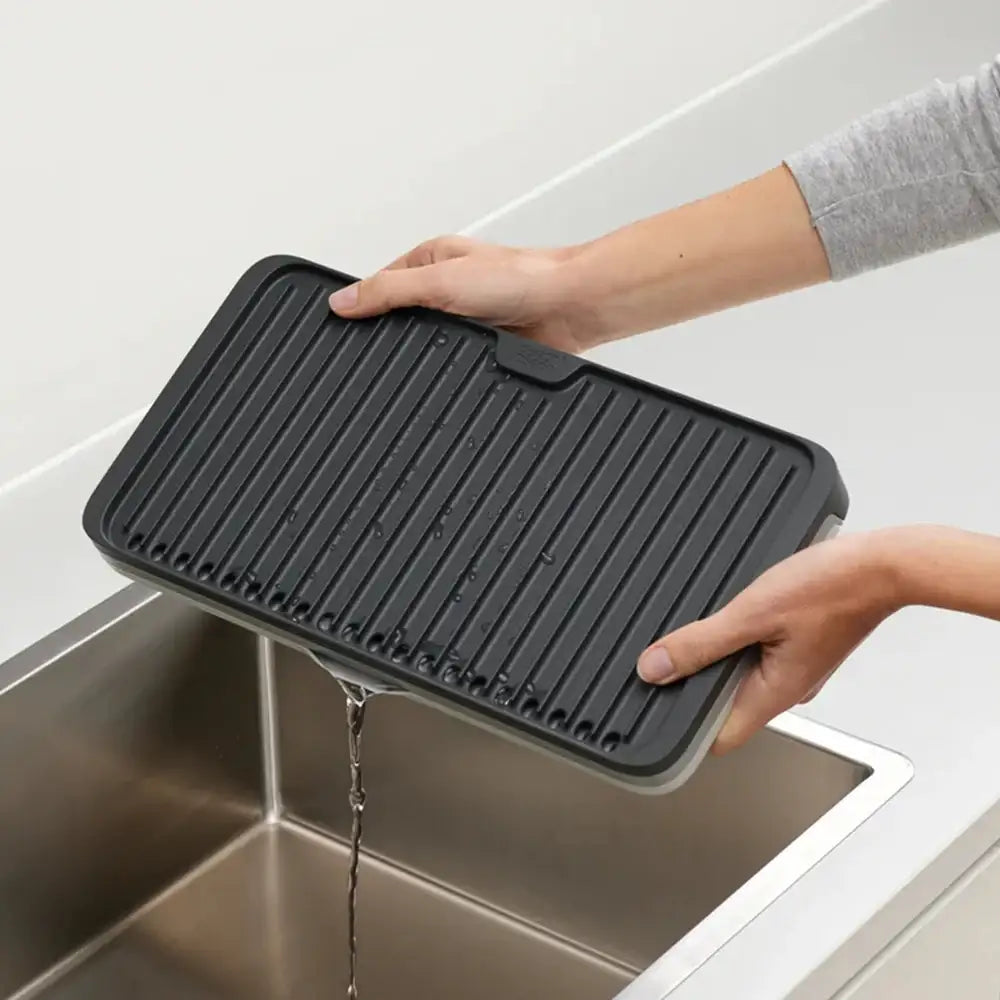 Person holding a black dish draining mat over a sink