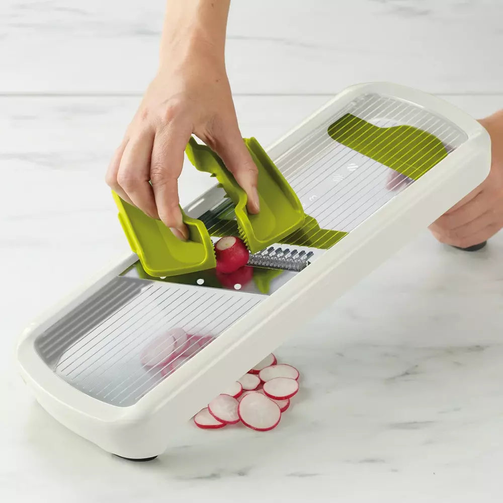 Person using a mandoline slicer to slice radishes on a marble countertop.