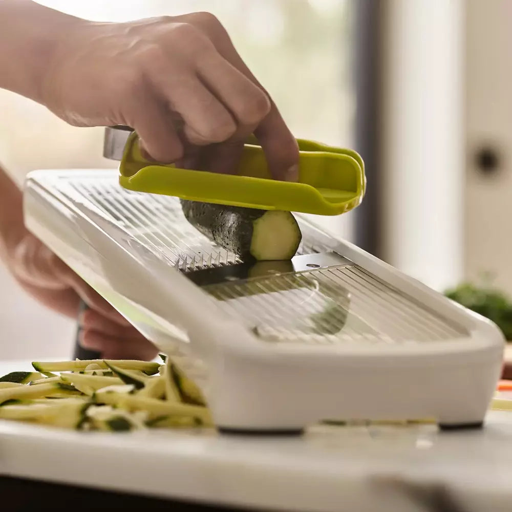 Person using a mandoline slicer to slice zucchini on a kitchen counter.
