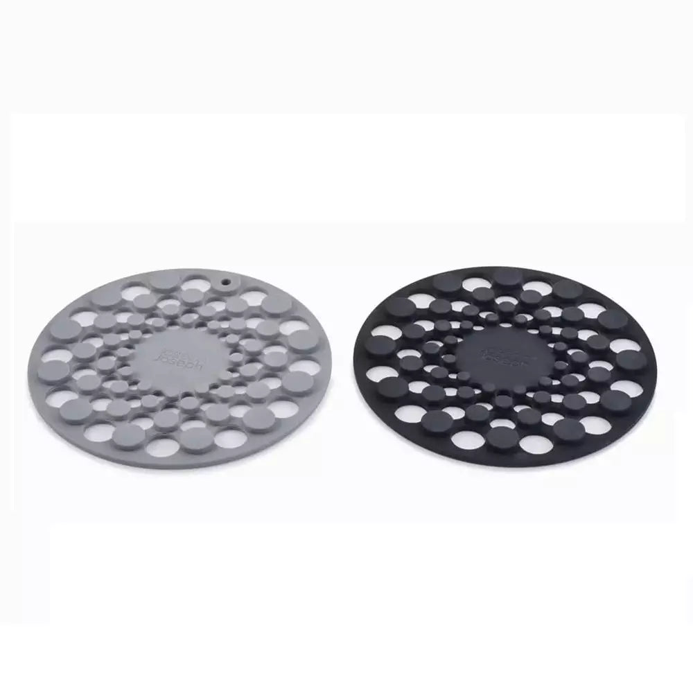 Two round silicone trivet mats with circular cutouts, shown side by side on a white background. One is gray and one is black, with the brand name 'JOSEPH JOSEPH' embossed in the center of each.