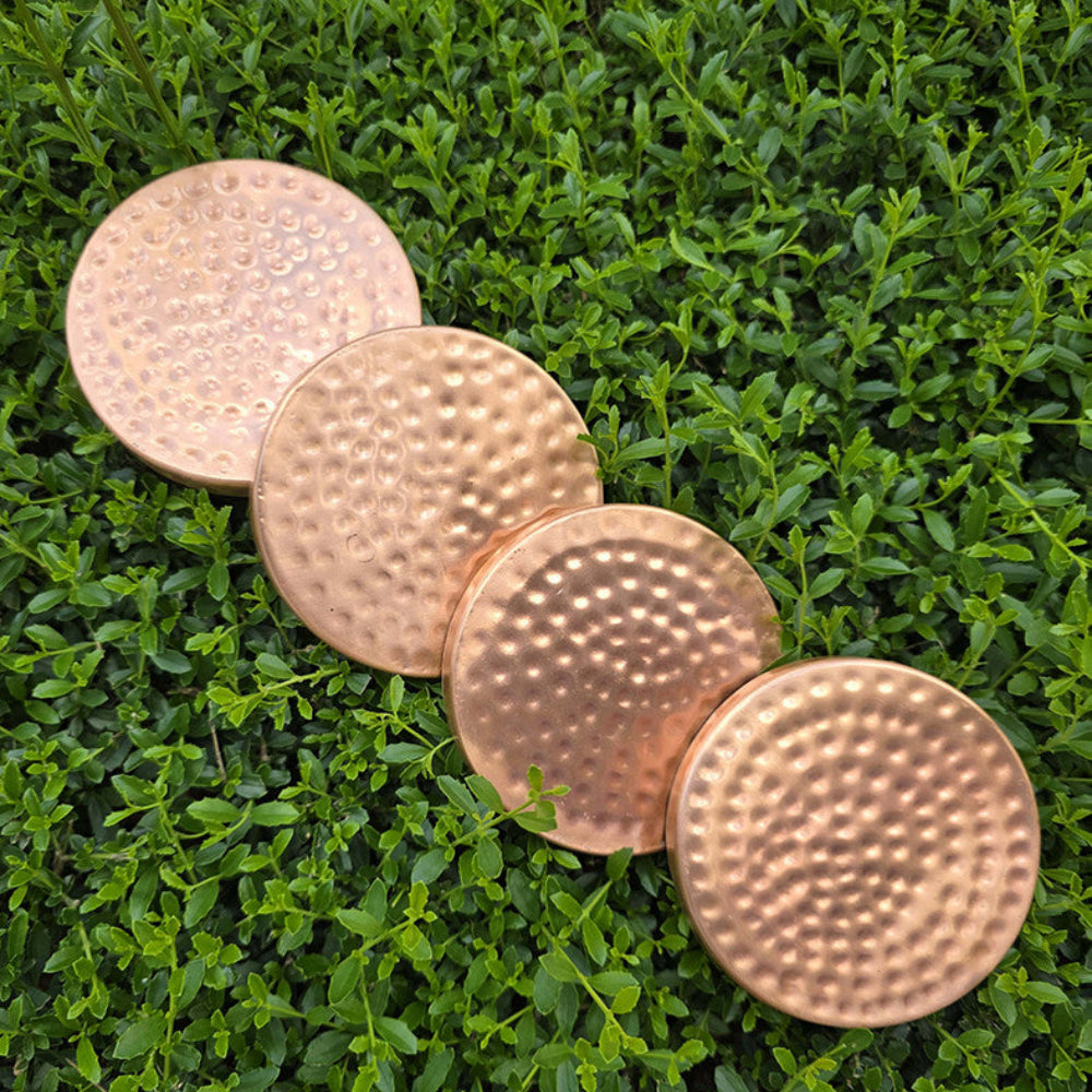 Four copper coasters on a grassy background