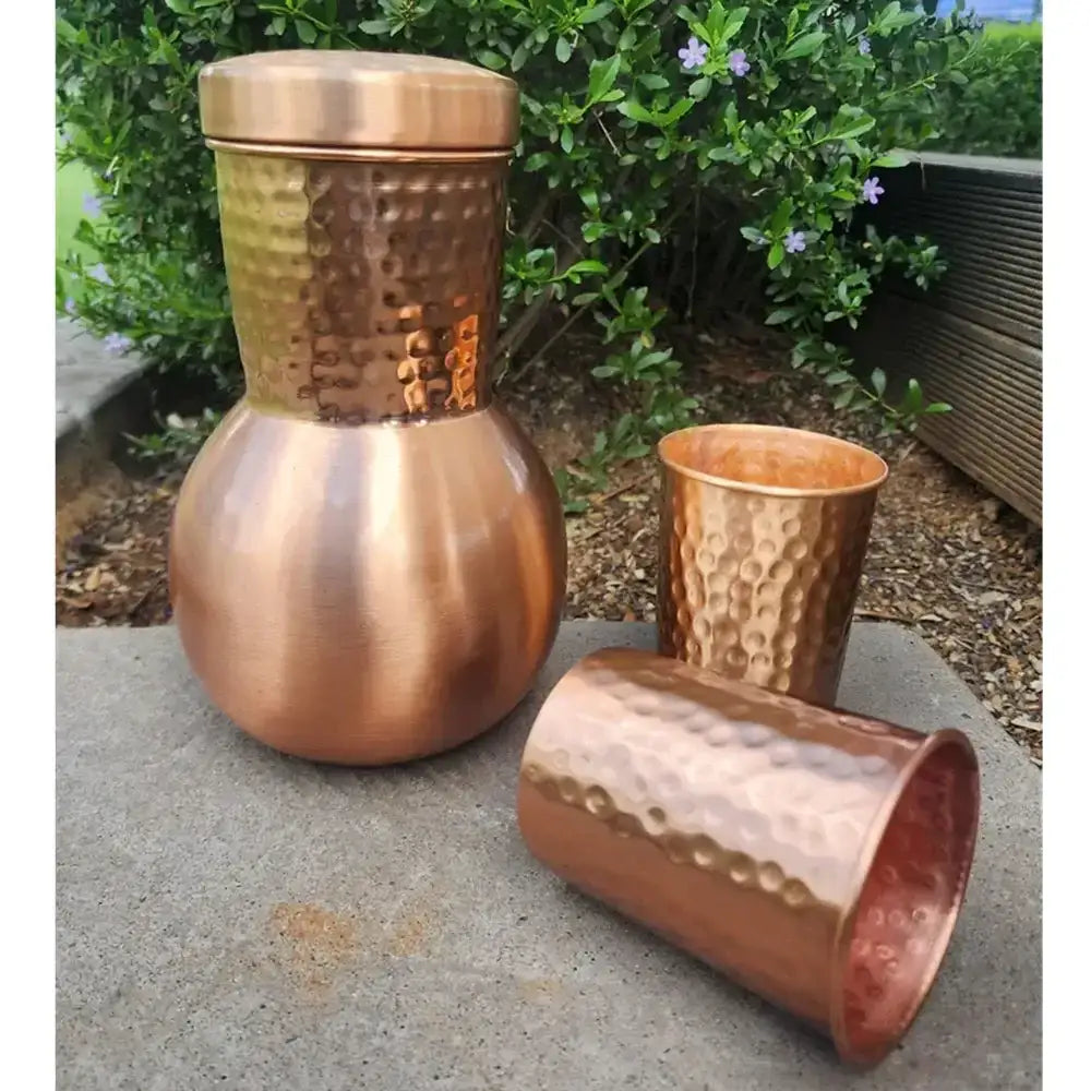 Set of copper tumblers on a concrete surface with greenery in the background