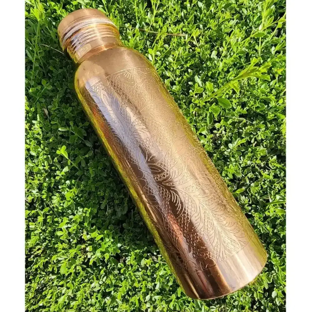 Copper water bottle with engraved design on a grass background