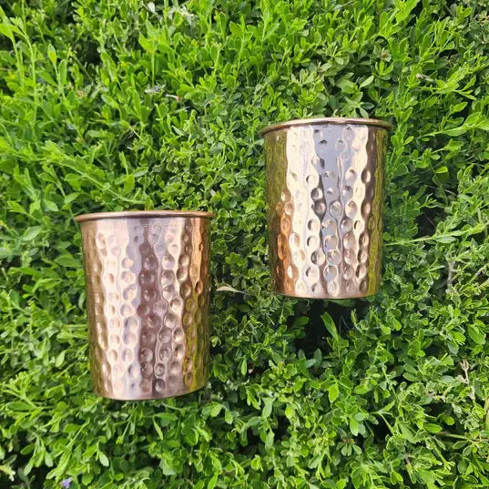 Two hammered copper cups on a green leafy background